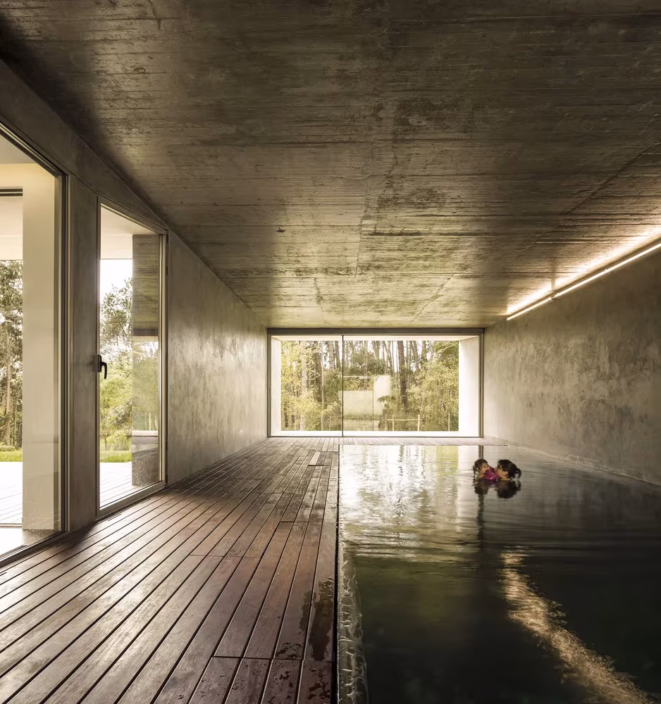 Piscina interior de la Hill Cork House con techo de hormigón, tarima de madera y ventanal al fondo