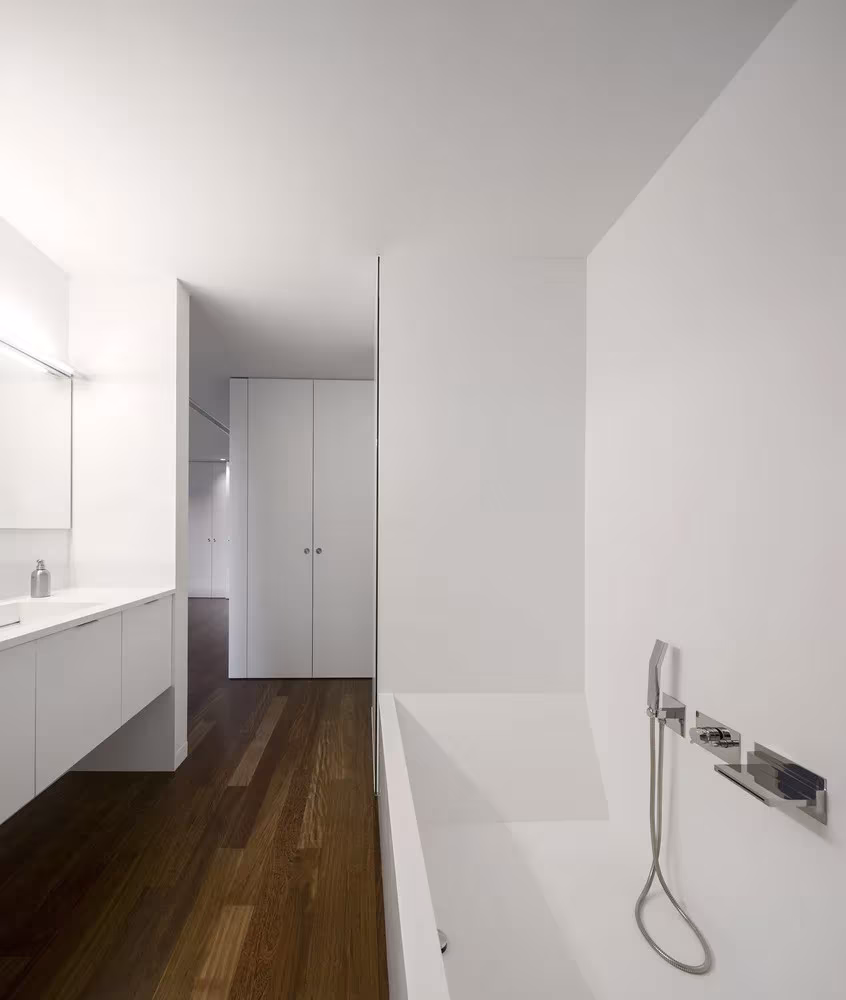 Baño blanco de la Hill Cork House con bañera exenta, grifería de pared y suelo de madera oscura