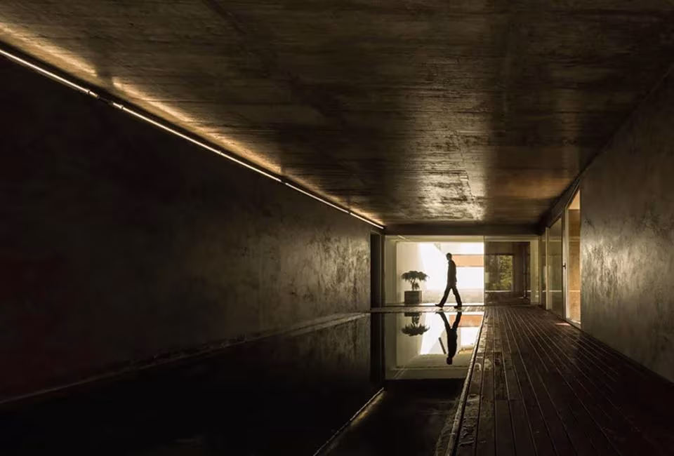 Lámina de agua alargada y oscura en la Hill Cork House con una figura reflejada al fondo