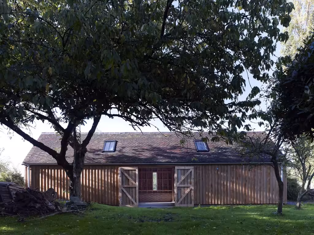 Fachada del Long Sutton Studio con portones de madera abiertos bajo un gran árbol en el césped