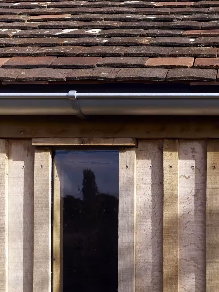 Detalle de alero con tejas, canalón y revestimiento de tablas de madera del Long Sutton Studio