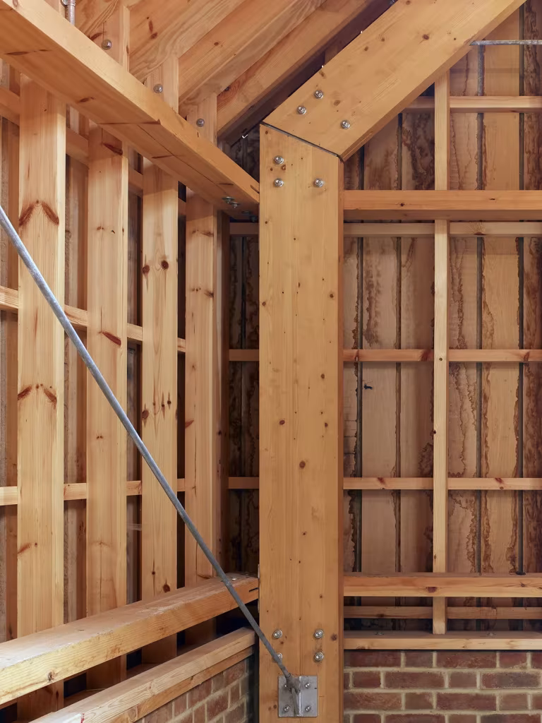 Esquina interior del Long Sutton Studio con estructura de madera, tirante de acero y zócalo de ladrillo