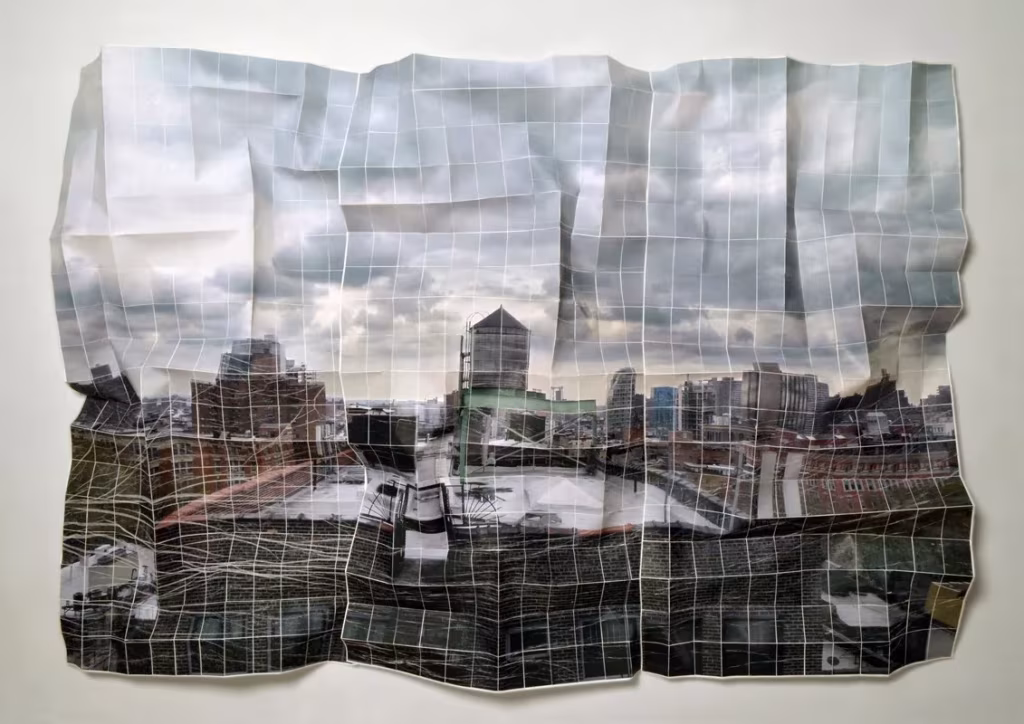 Panorámica urbana bajo cielo nublado impresa en papel arrugado y cuadriculado, de la serie Deconstruyendo ciudades