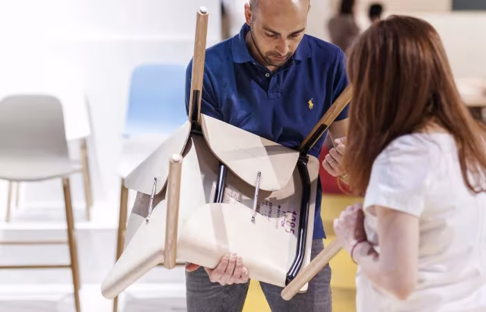 Dos personas examinan una silla Hide Chair de Kristalia con el respaldo de cuero en una feria