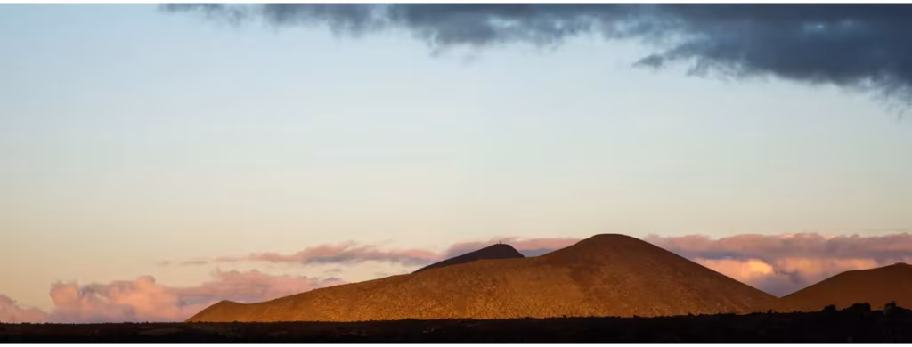 Volcanes de Timanfaya en Lanzarote iluminados por el sol del atardecer bajo un cielo con nubes