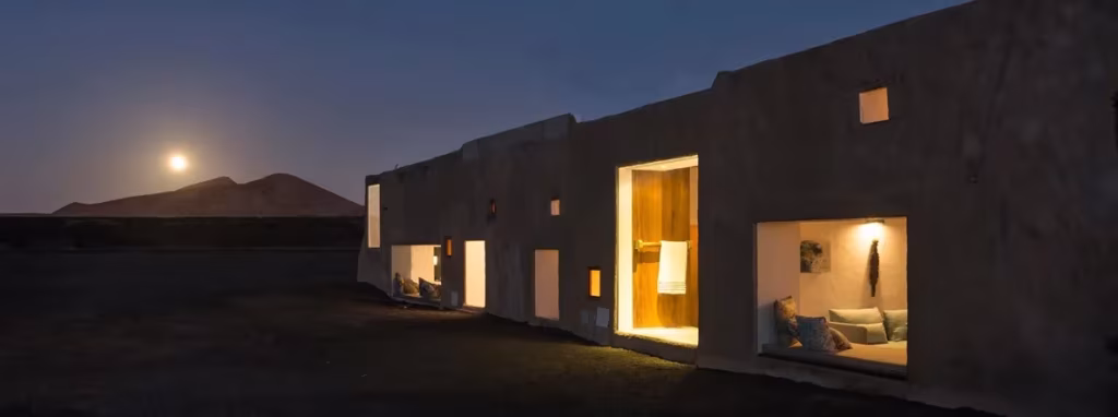 Buenavista Suites al anochecer con huecos iluminados en la fachada y la luna sobre un volcán