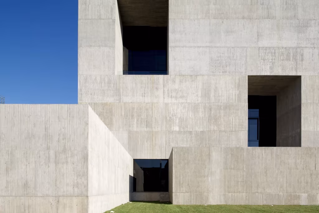 Fachada maciza de hormigón del Centro de Innovación UC con grandes ventanas retranqueadas y cielo azul