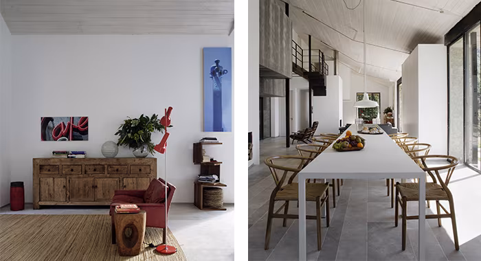 Rincón con aparador de madera y lámpara roja junto a un comedor con larga mesa blanca y sillas de madera