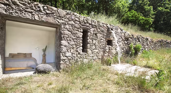Muro de piedra seca del antiguo establo con una gran abertura que deja ver un dormitorio entre la hierba