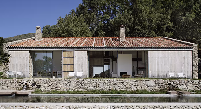 Antiguo establo rehabilitado como vivienda, con muros de piedra, cubierta de teja y un estanque en primer plano