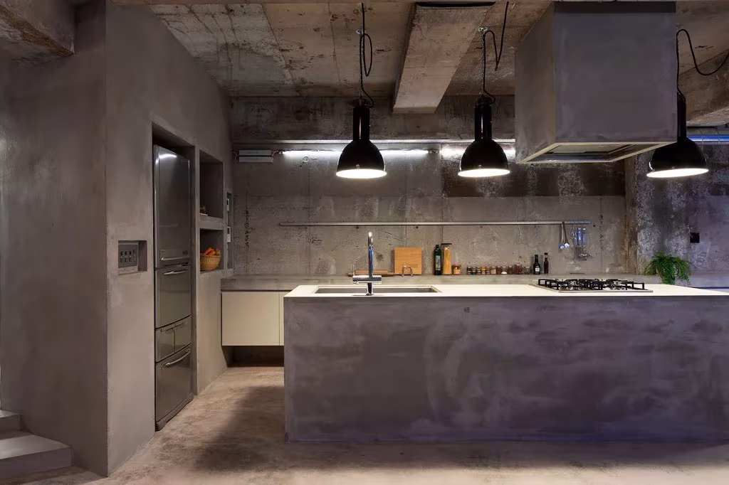 Cocina con isla de microcemento, campana cúbica y tres lámparas negras colgantes en el piso de Tokio