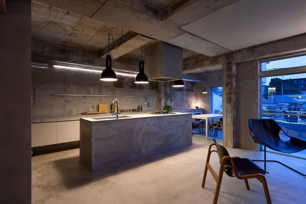 Isla de cocina de microcemento y butaca de madera junto al ventanal del apartamento de Jiyugaoka