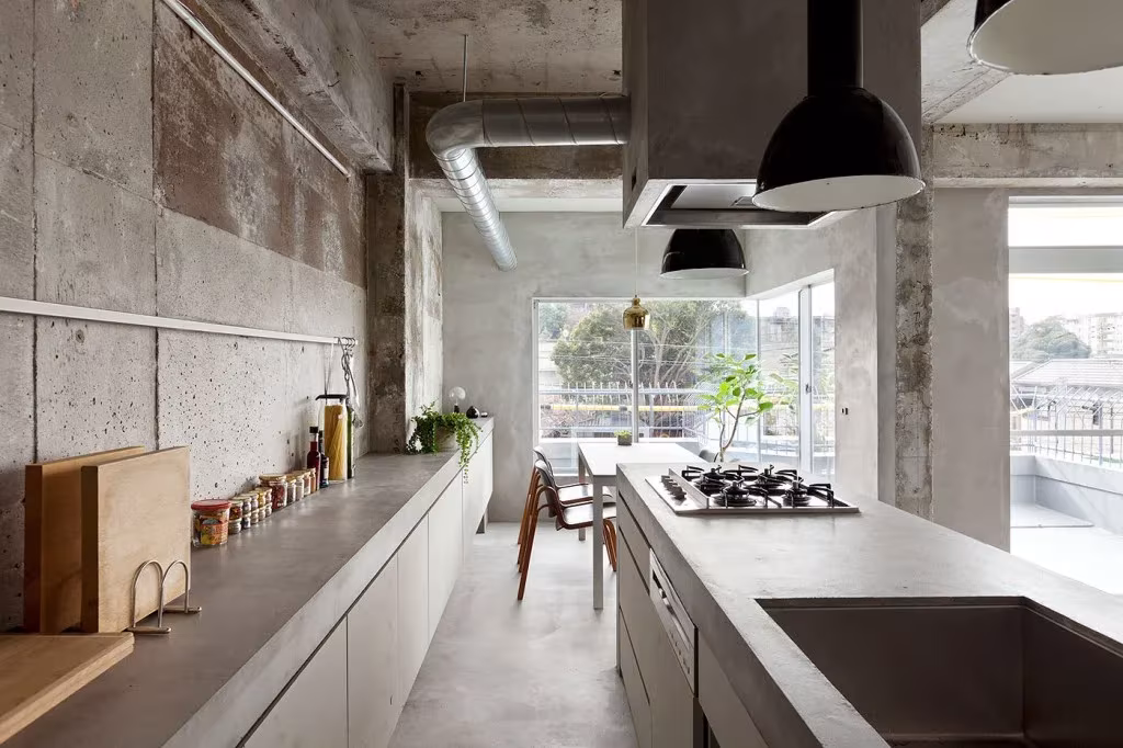 Cocina lineal con encimeras de acero, placa de gas y lámparas negras bajo un techo de hormigón