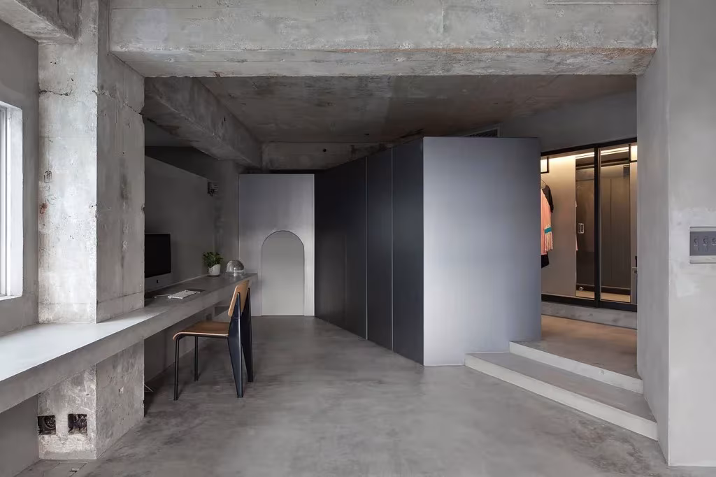 Estancia de hormigón en bruto con escritorio corrido y volumen gris del vestidor en el piso de Tokio