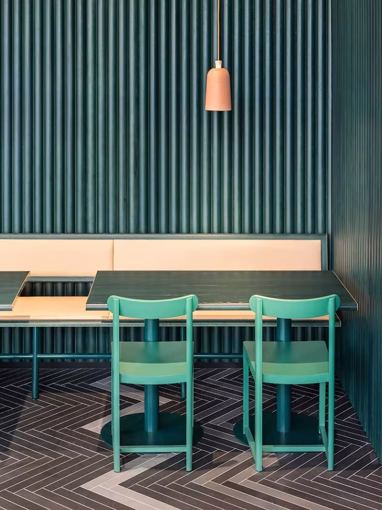Banco corrido con sillas color menta, paredes verde oscuro acanaladas y lámpara coral en un restaurante de Estocolmo