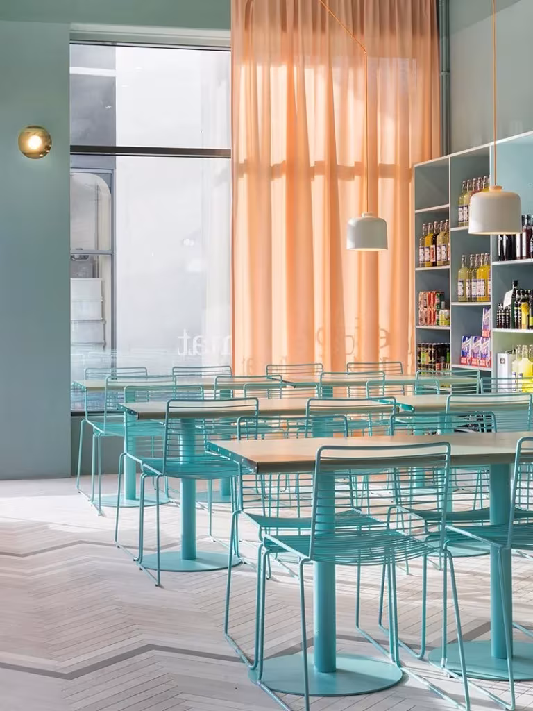 Comedor de Fine Food en Estocolmo con sillas de alambre turquesa, cortinas coral y estanterías de producto