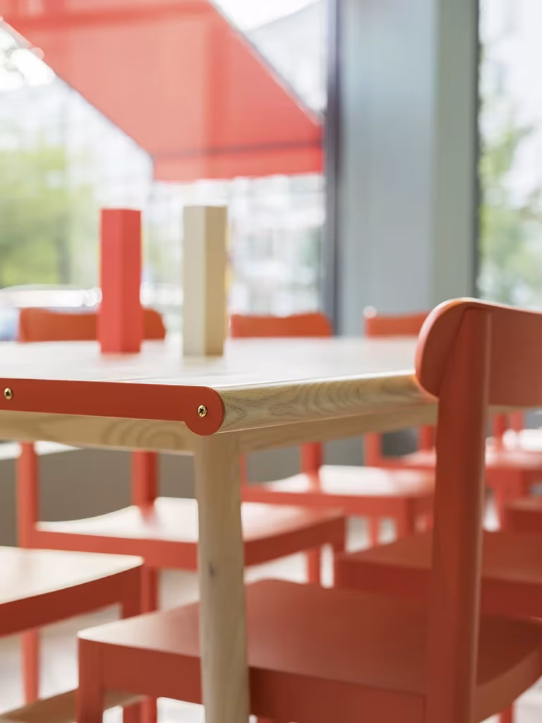 Detalle de mesa de madera clara con sillas coral junto al ventanal del restaurante de Note Design