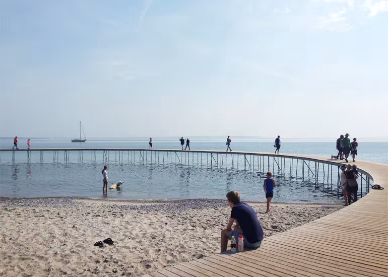 Puente circular de madera de Gjøde & Povlsgaard sobre el mar en Aarhus, con gente paseando y una playa
