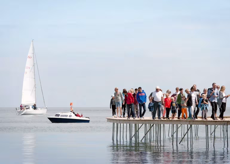 Grupo de personas sobre el puente sin fin de Aarhus con un velero y una lancha en el mar