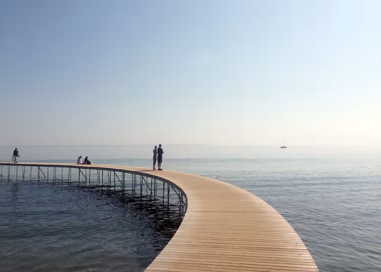 Pasarela curva de madera del puente sin fin de Aarhus adentrándose en un mar en calma