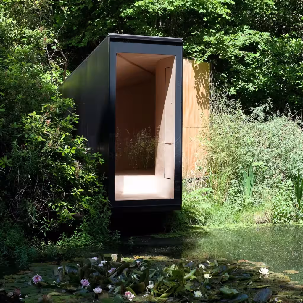 Forest Pond House de TDO Architecture, cabaña negra con interior de madera sobre un estanque en el bosque