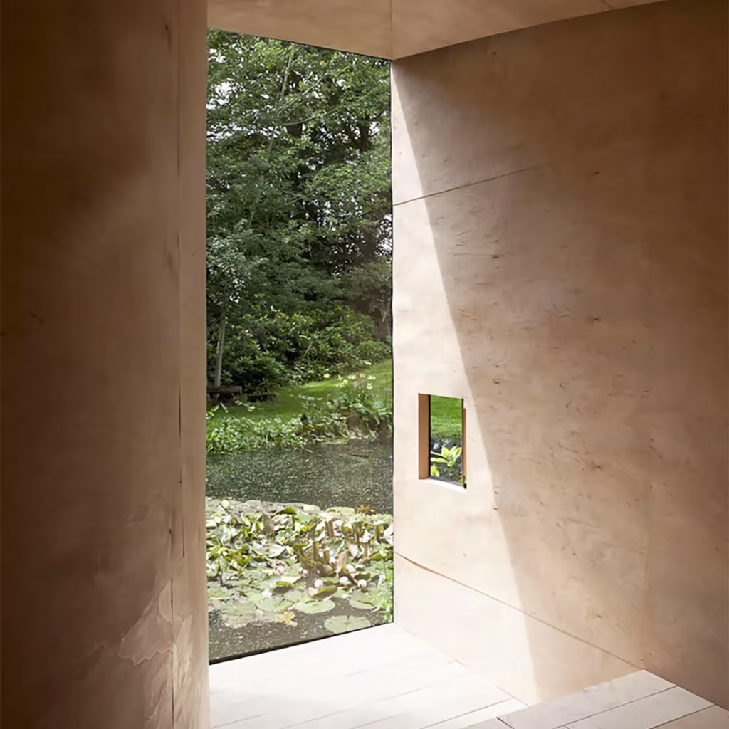 Interior de contrachapado de la Forest Pond House con ventanal abierto al estanque de nenúfares