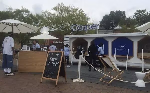 Tráiler de The Nap Tour instalado en un parque con sombrillas, tumbonas y una pizarra junto a la entrada