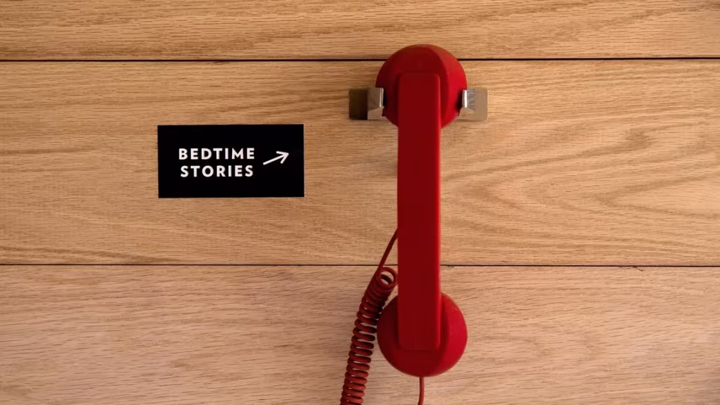 Teléfono rojo colgado en una pared de madera junto a un cartel de cuentos para dormir