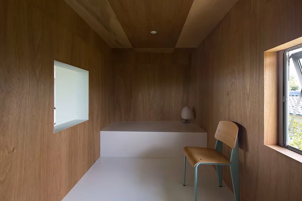Habitación forrada de madera en la casa Ohno con silla, banco blanco y ventanas hacia el huerto