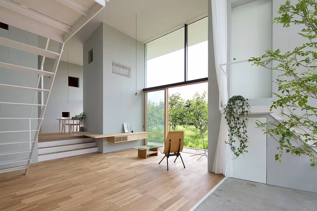 Salón de la casa Ohno con suelo de roble, escalera blanca, butaca y ventanal hacia el huerto