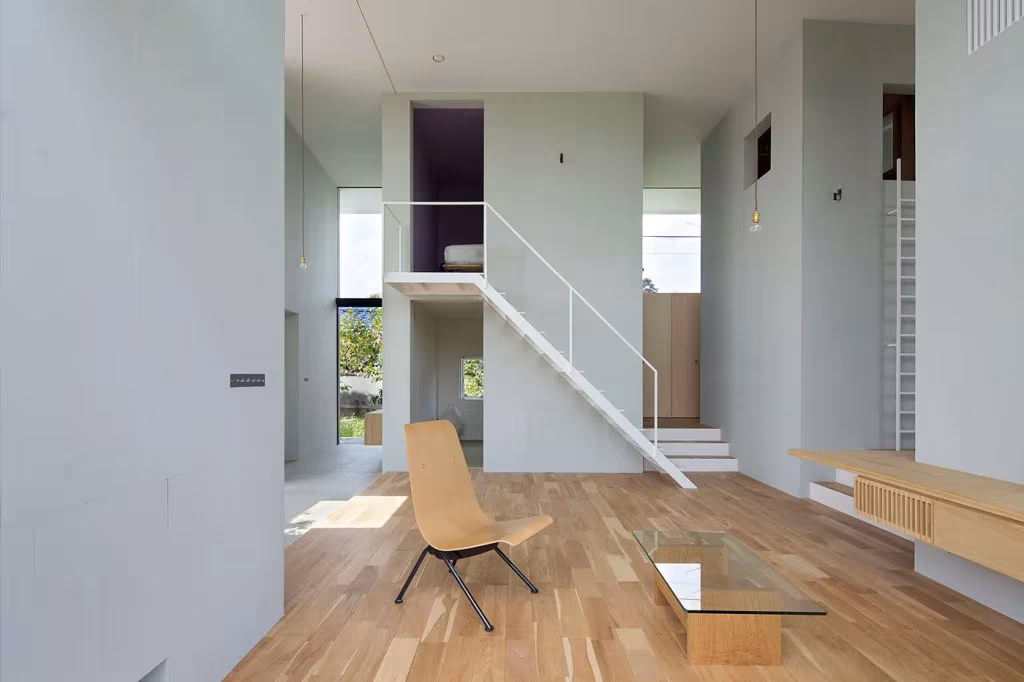 Interior blanco de la casa Ohno con altillos, escalera de acero, silla de madera y mesa baja de vidrio