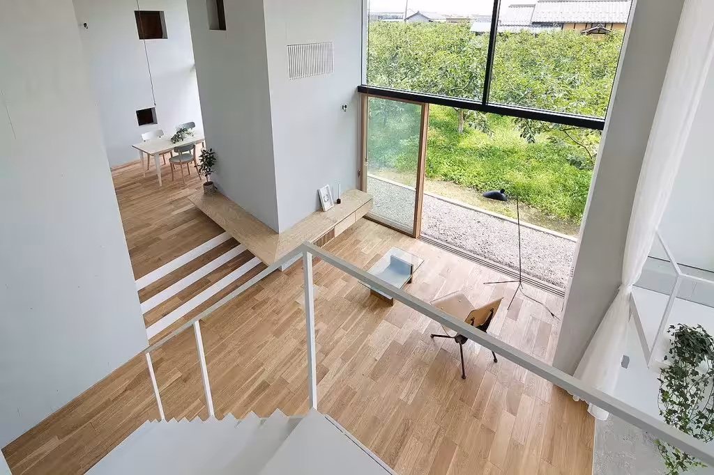 Vista desde la escalera de la casa Ohno hacia el salón con suelo de madera y gran ventanal al huerto