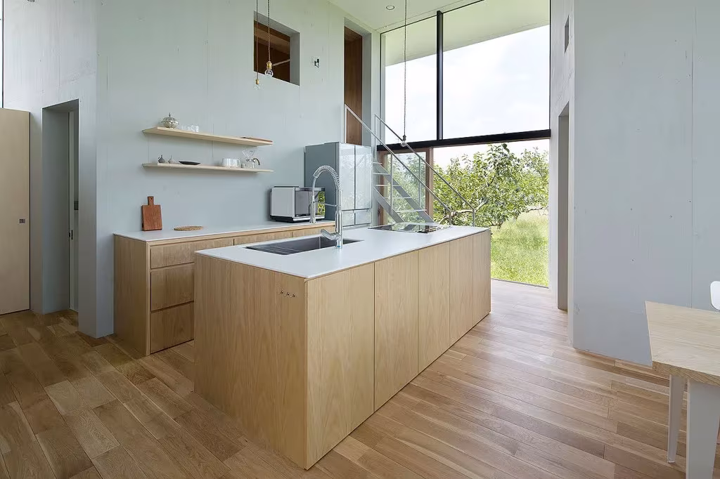 Cocina de la casa Ohno con isla de madera clara, estantes flotantes y ventanal al jardín