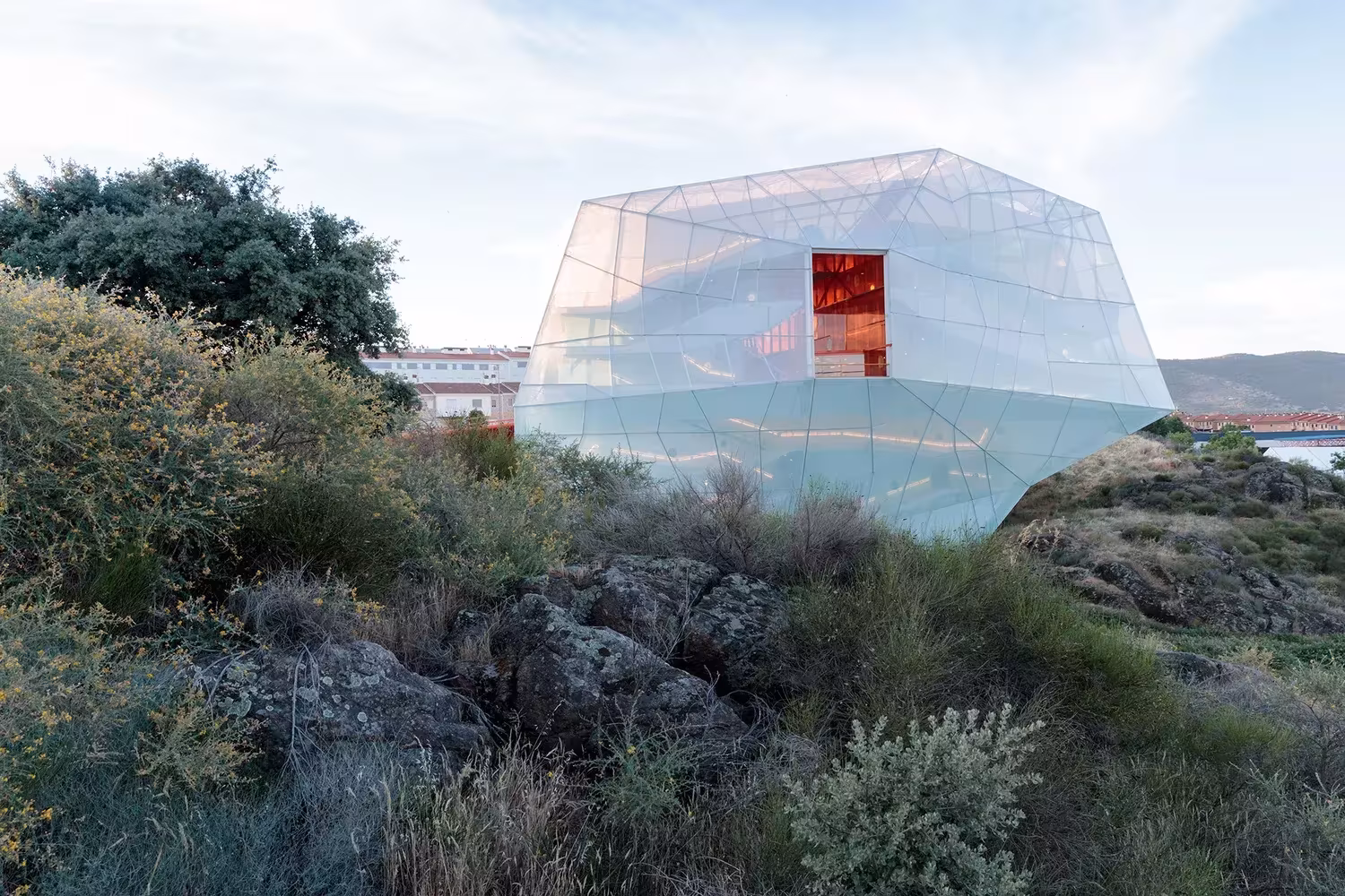 Palacio de Congresos de Plasencia de Selgas Cano, volumen translúcido posado sobre la ladera entre matorral