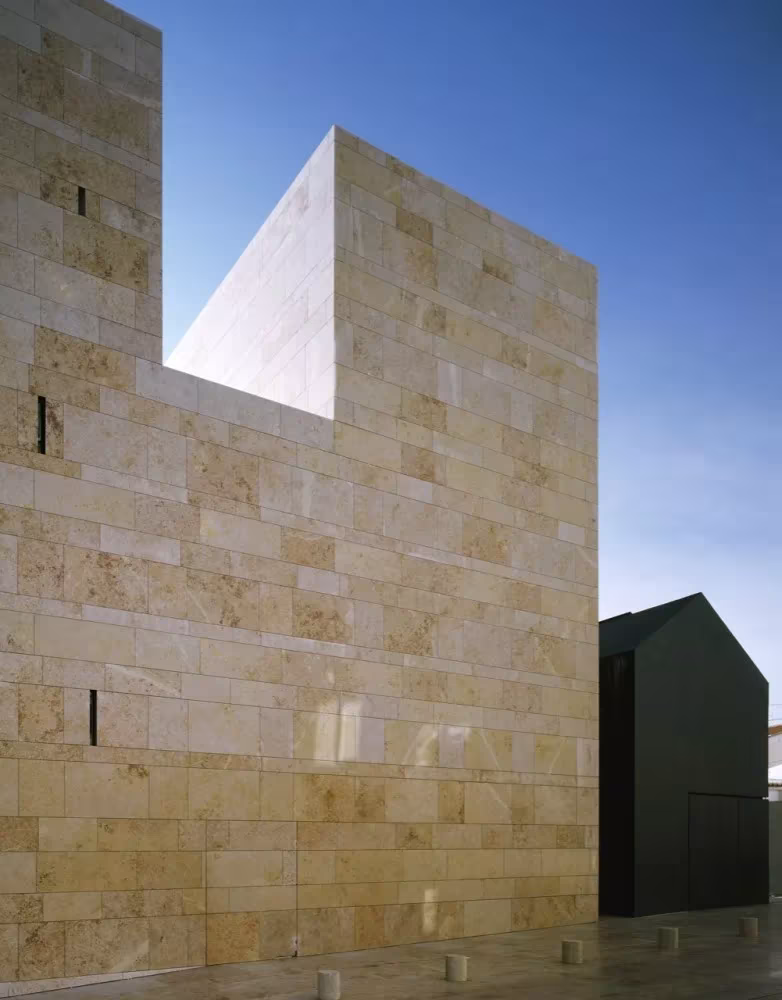 Volumen de piedra caliza del Centro de Artes de Sines de Aires Mateus con un hueco recortado contra el cielo azul