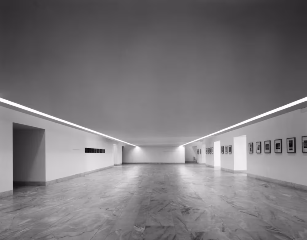 Sala de exposiciones alargada del Centro de Artes de Sines con fotografías en las paredes y luz perimetral en el techo