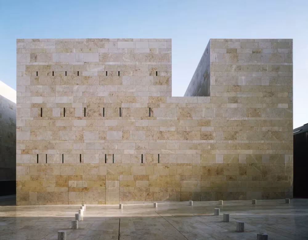 Fachada de piedra dorada con pequeñas aberturas del Centro de Artes de Sines, como una muralla contemporánea
