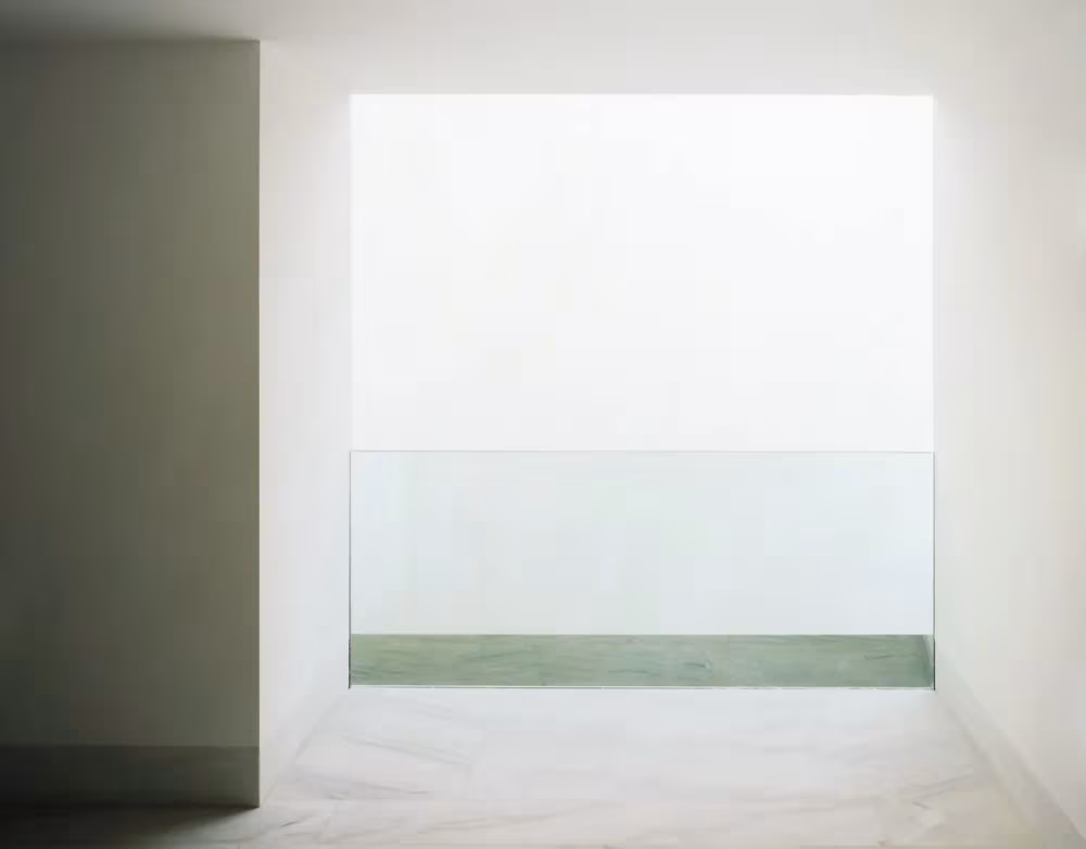 Espacio blanco y luminoso con un antepecho de vidrio frente a un gran hueco de luz en el Centro de Artes de Sines