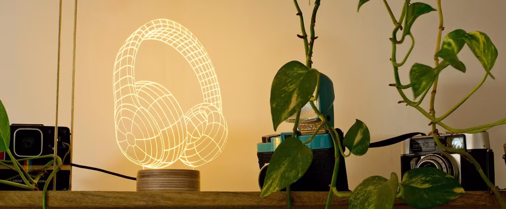 Lámpara acrílica de Cheha Studio con forma de auriculares iluminados junto a plantas en una repisa