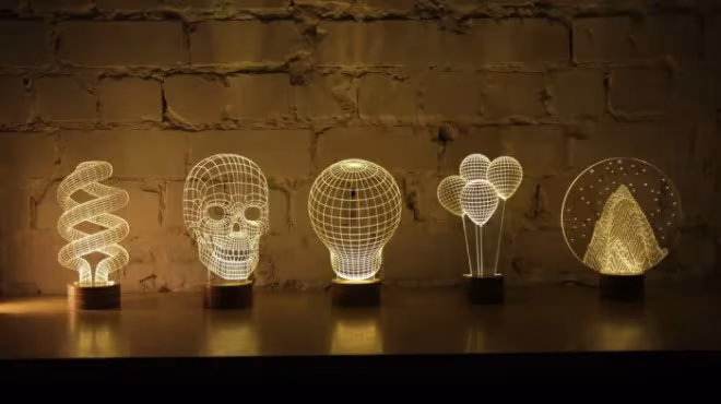 Lámparas acrílicas grabadas con forma de calavera, bombilla y globos iluminadas ante un muro de ladrillo