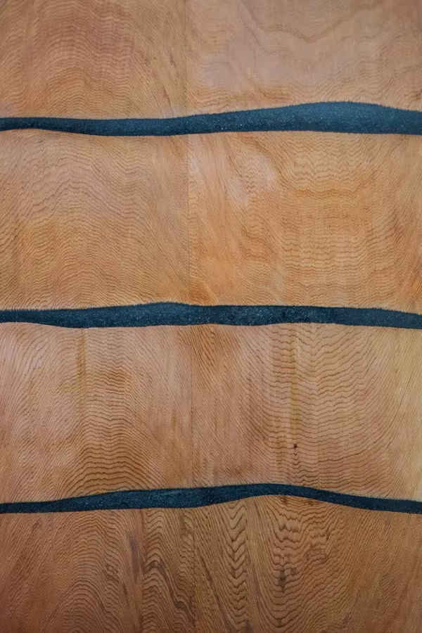 Primer plano de la veta del cedro atravesada por franjas onduladas de resina negra en el mueble Fuse
