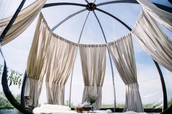 Vista hacia arriba desde el interior de la cúpula Oasis, con cortinas de lino colgando de los arcos y cielo azul