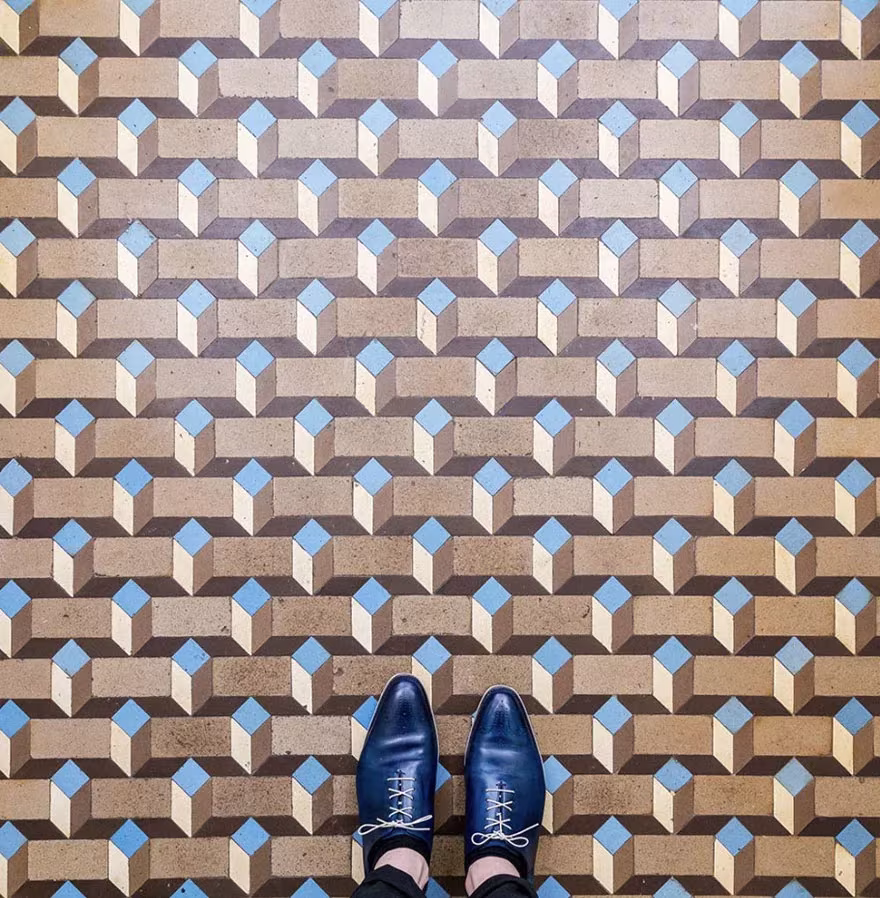 Suelo con patrón de cubos en relieve en tonos marrones y azules bajo unos zapatos azules