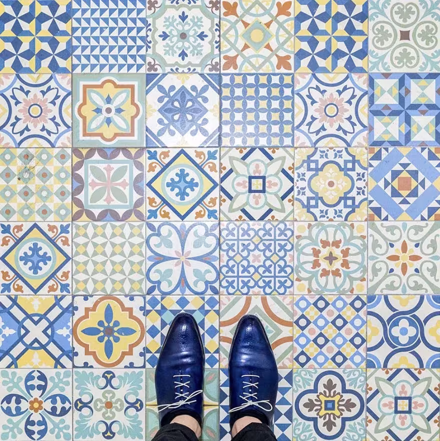 Mosaico de baldosas hidráulicas azules y amarillas de distintos diseños con zapatos azules encima