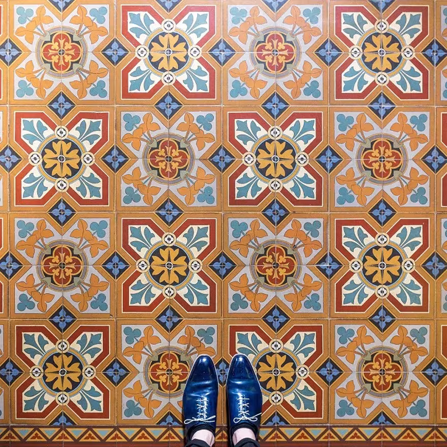 Suelo hidráulico ocre con rosetones azules y rojos de inspiración geométrica y zapatos azules