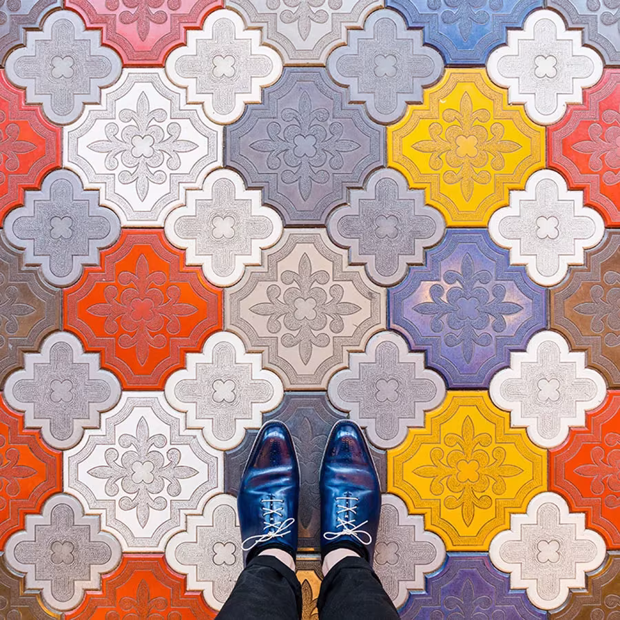 Baldosas lobuladas en relieve de colores gris, naranja, amarillo y lila bajo unos zapatos azules