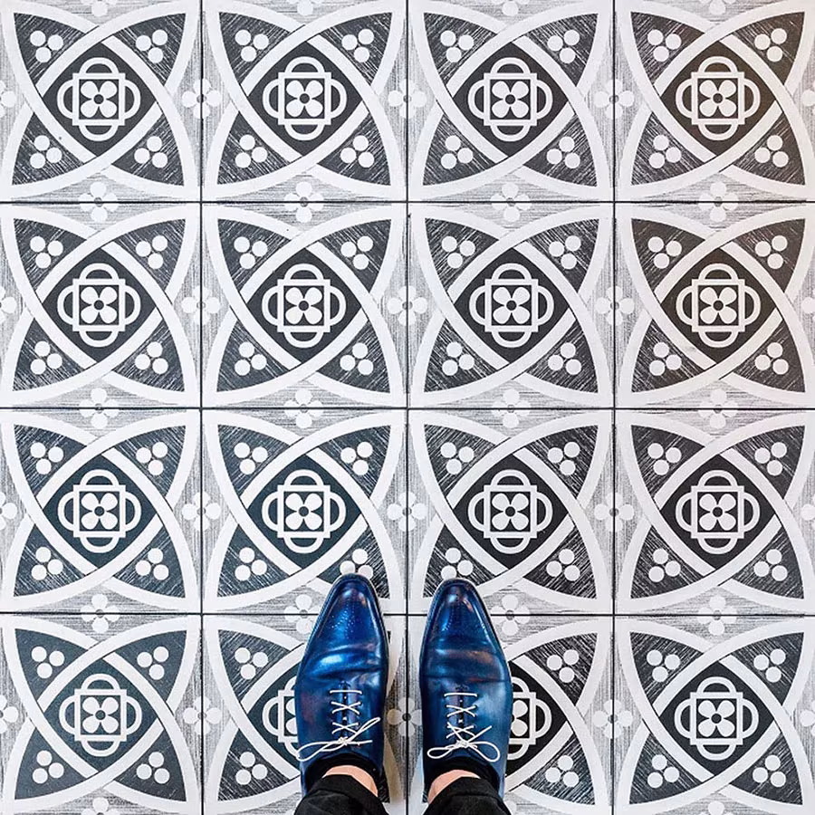 Baldosas grises y blancas con motivos góticos de círculos y pétalos bajo unos zapatos azules