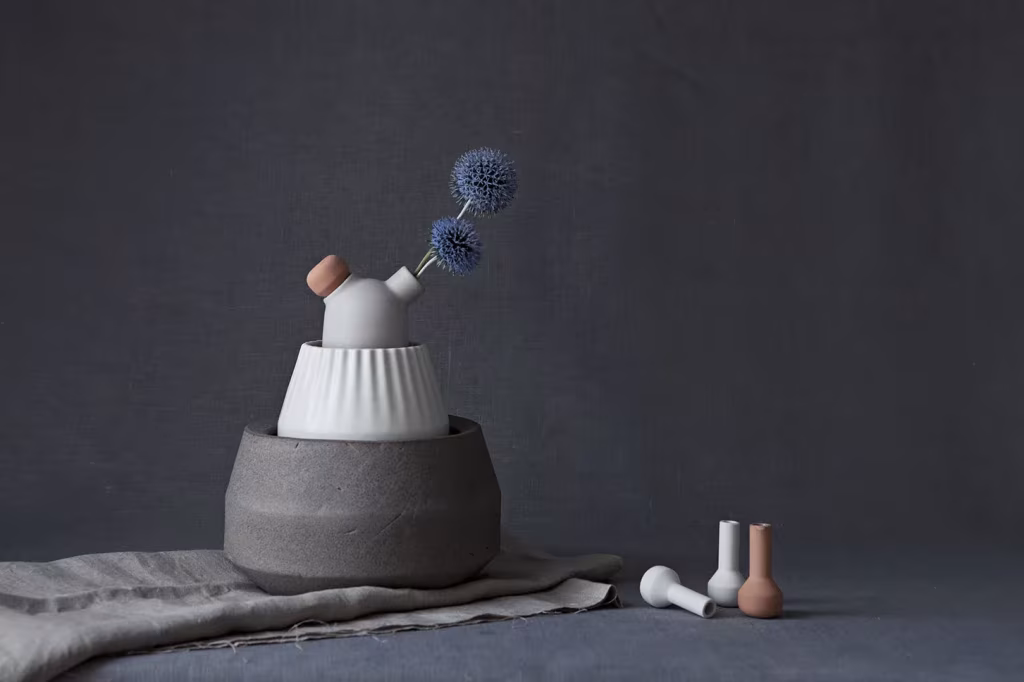 Jarrón Biophilia con flor azul de cardo sobre base de hormigón y pequeñas piezas de cerámica