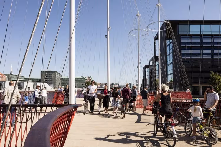 Peatones y ciclistas cruzando Cirkelbroen entre sus mástiles en un día soleado
