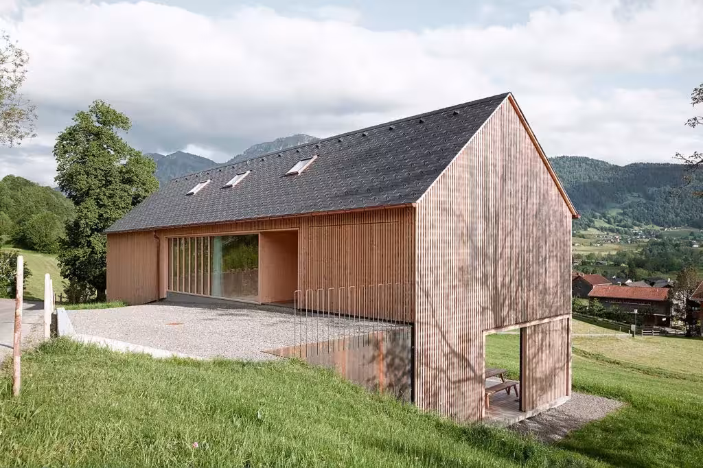 Casa de Julia y Björn de Innauer-Matt con fachada de madera y tejado a dos aguas en un prado de Egg